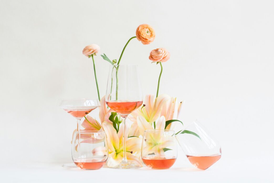 glasses of rosé wine among a small display of spring flowers on a white backdrop